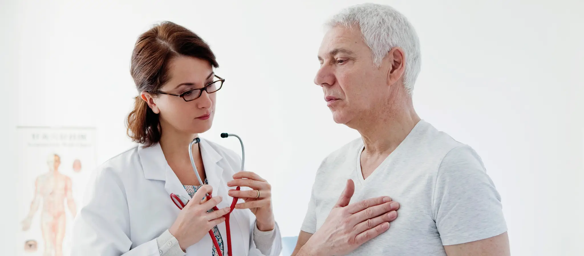 An elderly man is being examined by a doctor who is checking his chest with a stethoscope.